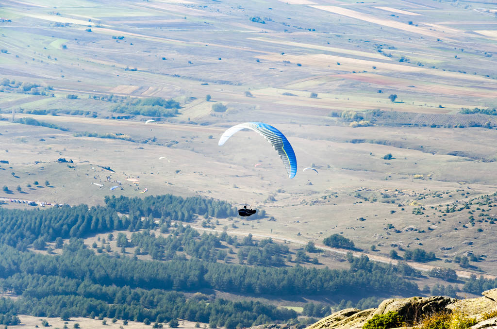 Näkymä laskuvarjohyppääjä lentää ilmassa yli laakson
 - Valokuva, kuva