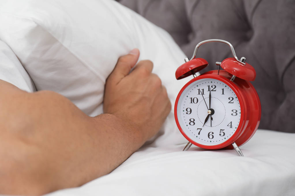 Alarm clock and man covering head with pillow in bedroom. Time of day - Photo, Image