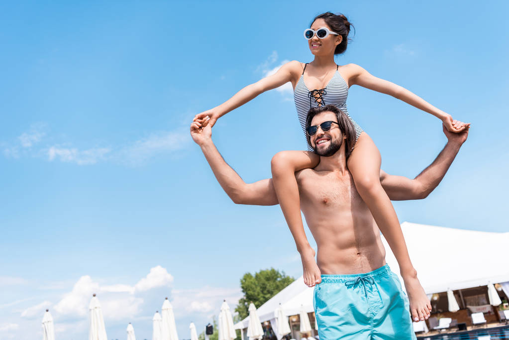 happy girl in swimsuit having fun and sitting on shoulders of her boyfriend - Photo, Image