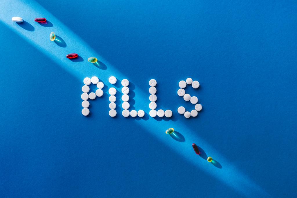 top view of lettering pills by white tablets on blue background with sunlight  - Photo, Image