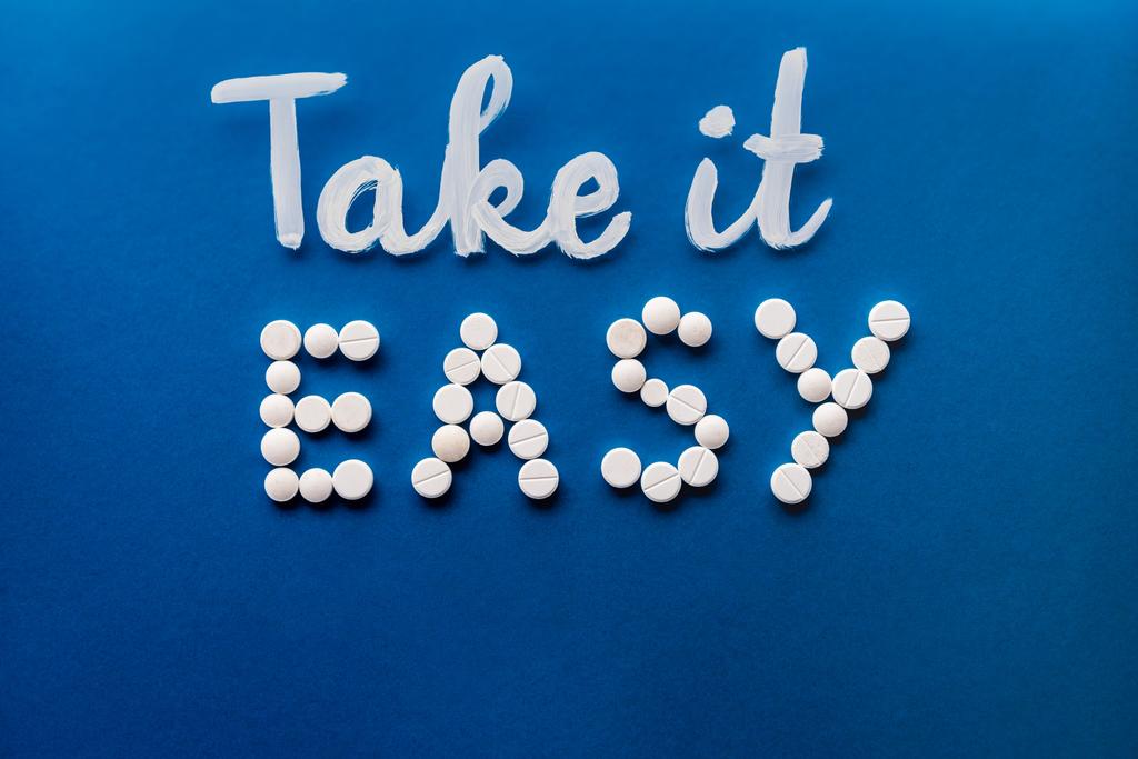 top view of lettering take it easy made by white pills on blue background  - Photo, Image