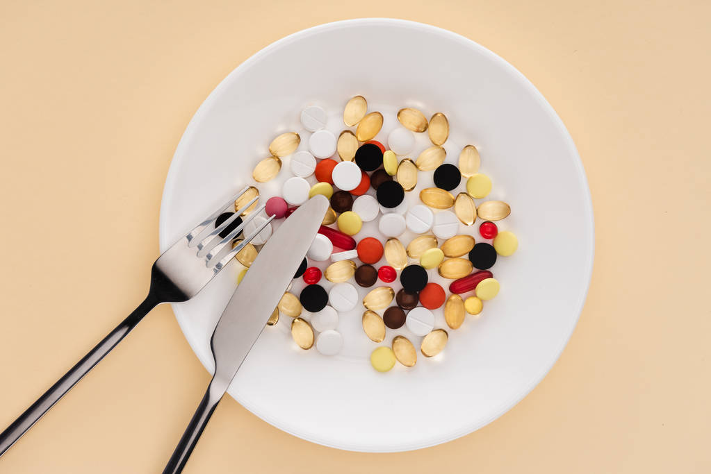 vista dall'alto di forchetta, coltello e piatto con varie pillole su sfondo beige
 - Foto, immagini