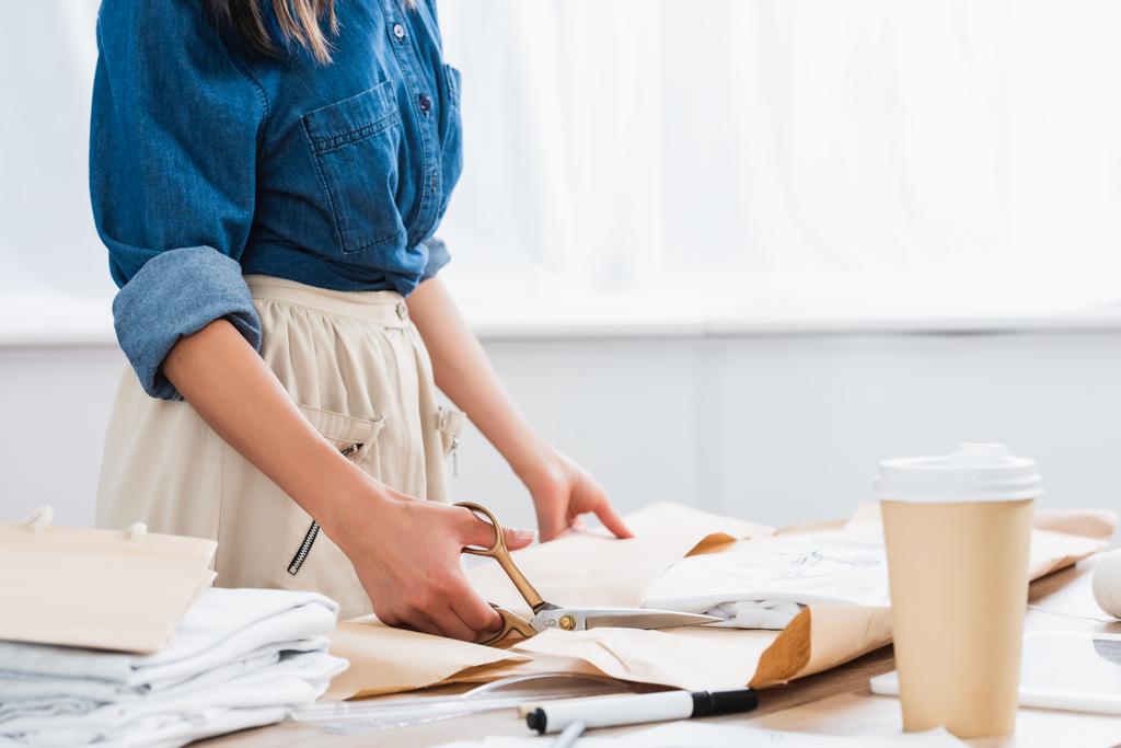przycięte zdjęcie kobiece projektanta mody, zawijanie t-shirt z nadrukiem w pakiecie papieru przy stole z filiżanki kawy - Zdjęcie, obraz