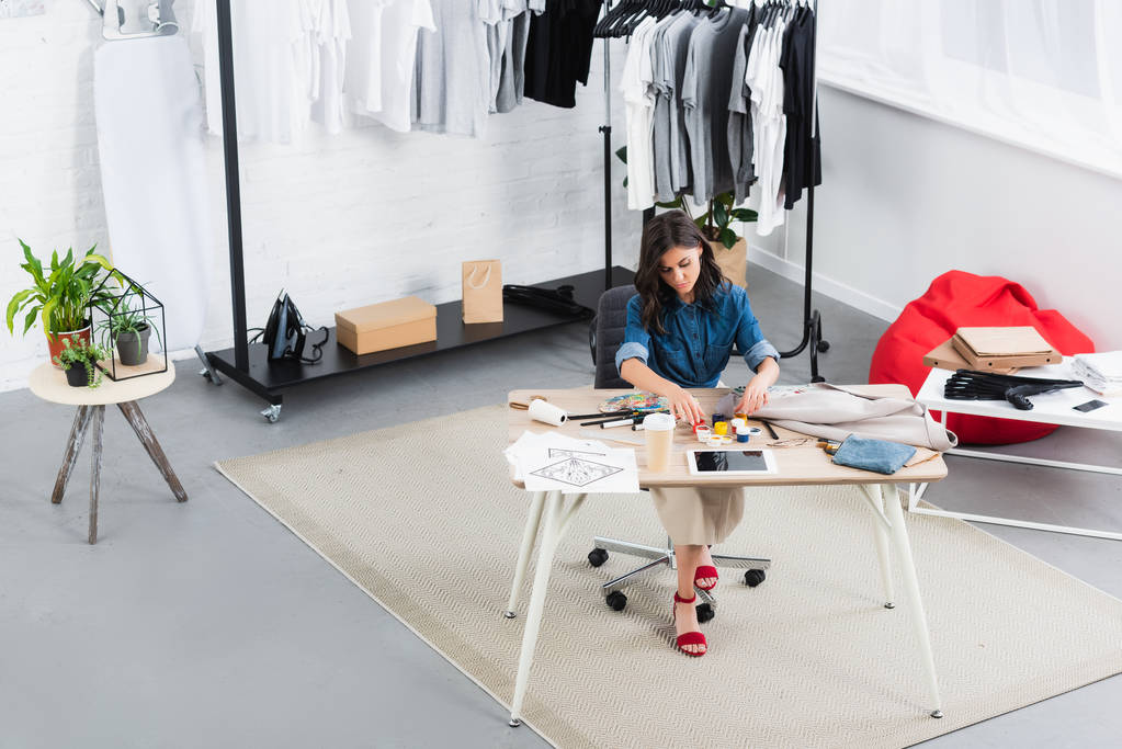 visão de alto ângulo da pintura de designer de moda feminina na jaqueta na mesa de trabalho no estúdio de design de roupas
 - Foto, Imagem