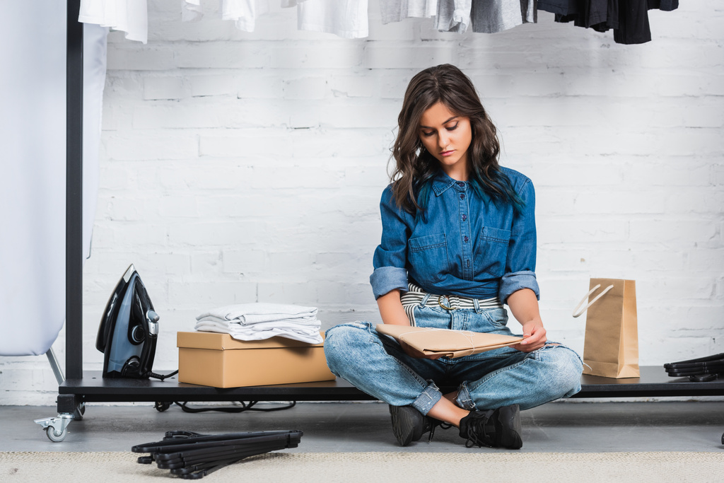 молодая дизайнерша сидит с бумажным пакетом в студии дизайна одежды
 - Фото, изображение