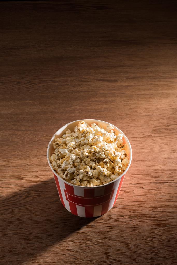 close up view of disposable bucket with popcorn on wooden tabletop - Photo, Image