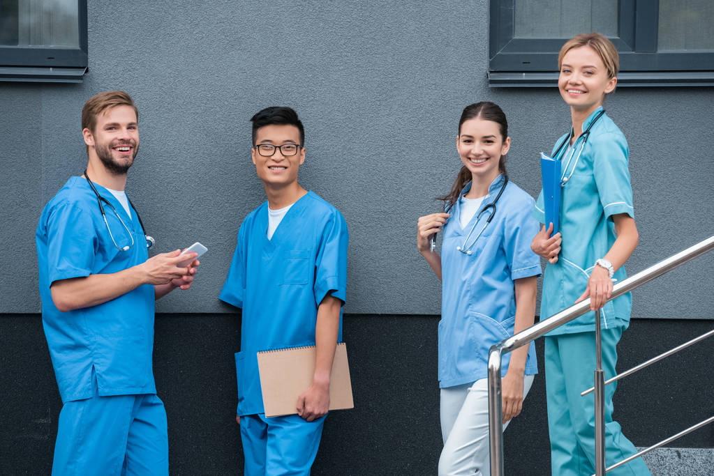 улыбающиеся мультикультурные студенты-медики, смотрящие в камеру возле медицинского университета
  - Фото, изображение