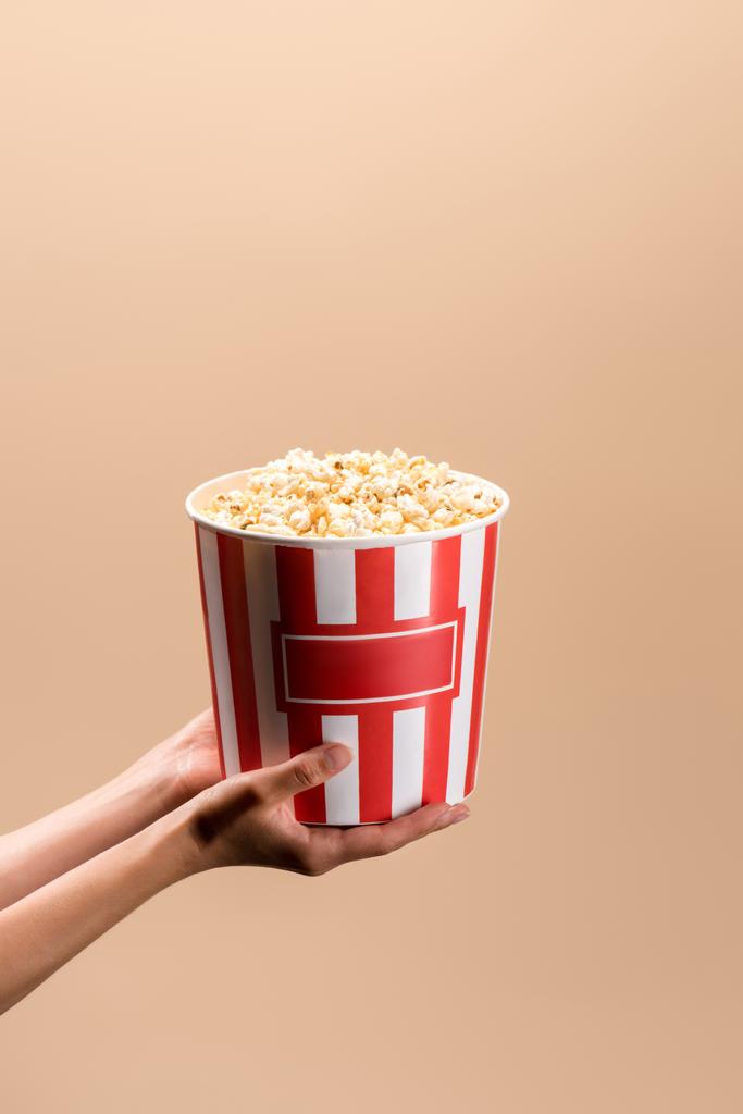 partial view of woman holding disposable bucket with popcorn isolated on beige - Photo, Image