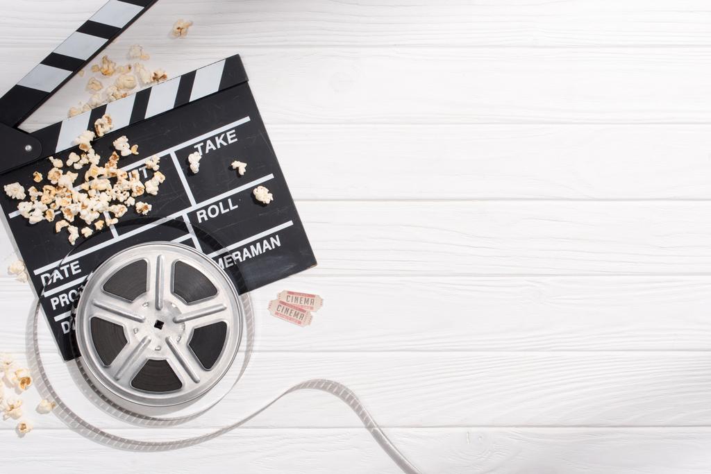 плоский уголок с доской для хлопка, фильмлентами, попкорном и билетами в ретро-кино на белой деревянной столешнице
 - Фото, изображение