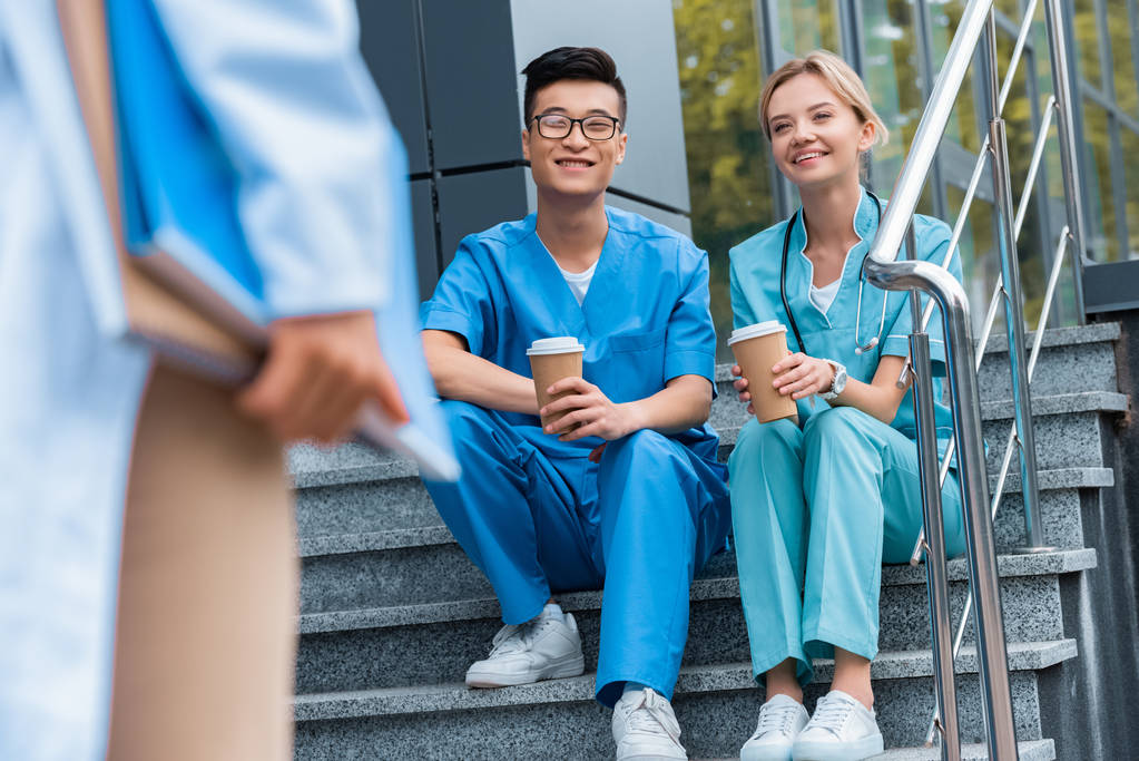 ořízne obraz učitele při pohledu na usmívající se studenty medicíny sedí na schodech s kávou i jít  - Fotografie, Obrázek