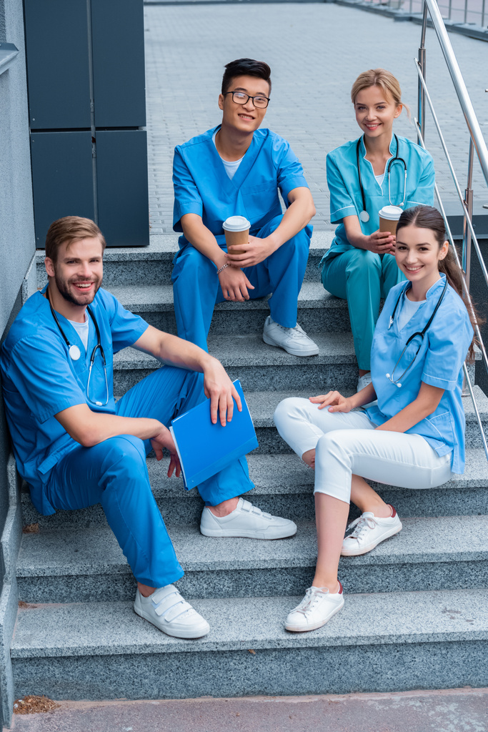 uśmiechający się wielokulturowym studentów medycyny, siedząc na schodach i patrząc na kamery - Zdjęcie, obraz