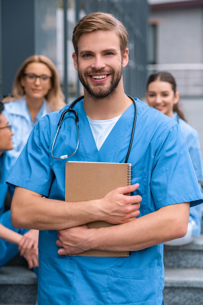 όμορφος Καυκάσιος φοιτητής ιατρικής στέκεται με το σημειωματάριο και να βλέπουν τα φωτογραφικών μηχανών - Φωτογραφία, εικόνα