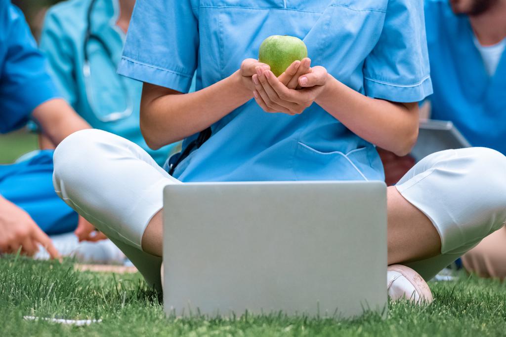 обрізане зображення студента-медика, який тримає стигле зелене яблуко в руках і сидить біля ноутбука
 - Фото, зображення