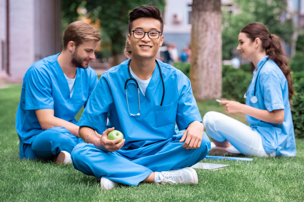 красивый азиатский студент-медик держит яблоко и смотрит в камеру
 - Фото, изображение