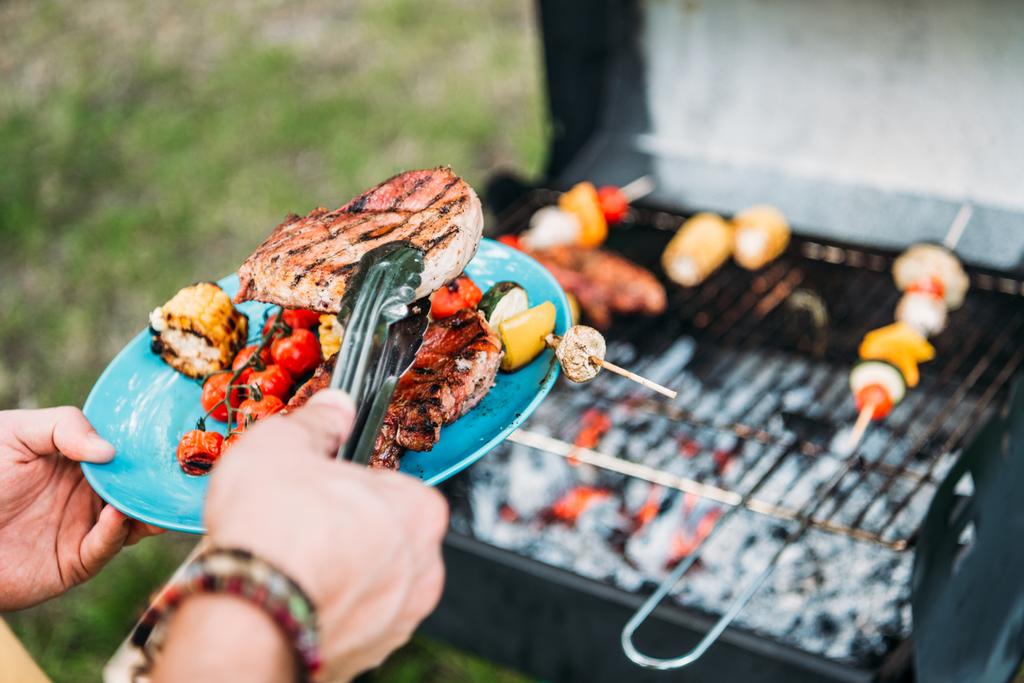 vista parziale dell'uomo con pinze che mettono cibo grigliato sul piatto durante il barbecue nel parco
 - Foto, immagini