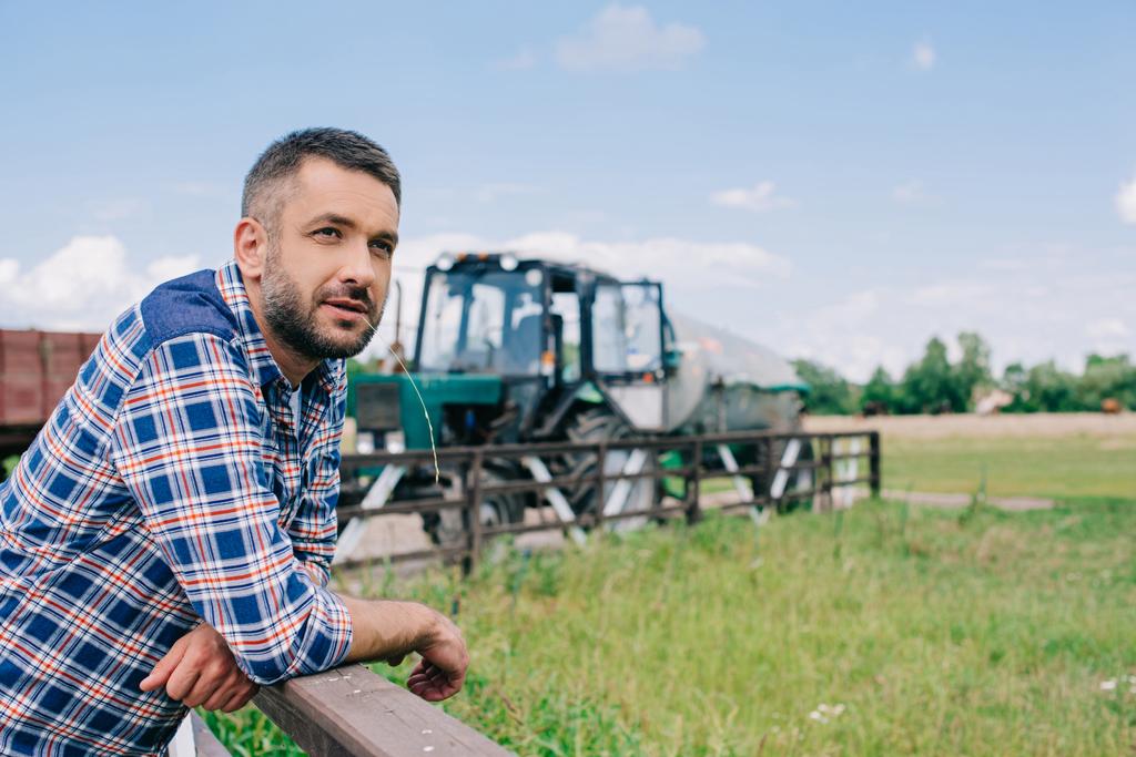 granjero de mediana edad pensativo apoyado en barandilla y mirando hacia otro lado en la granja
  - Foto, Imagen
