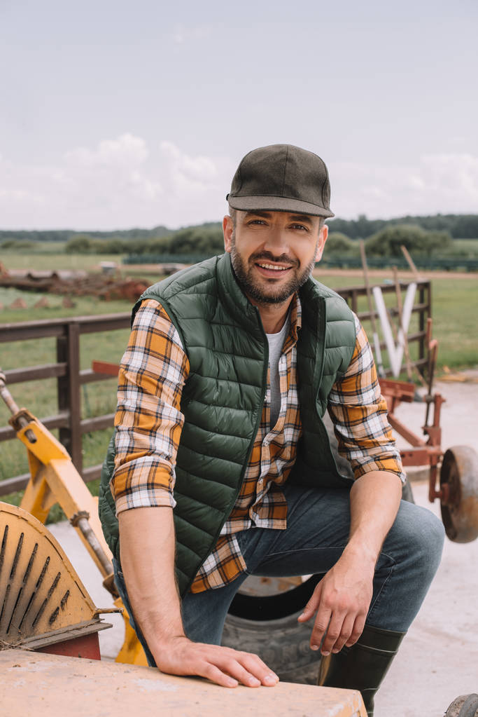 schöner Bauer mittleren Alters mit Mütze, der während seiner Arbeit auf der Ranch in die Kamera lächelt - Foto, Bild