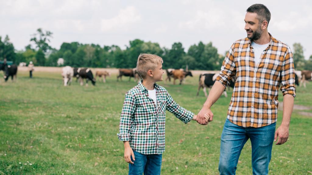 счастливые отец и сын держатся за руки и улыбаются друг другу на ферме
 - Фото, изображение