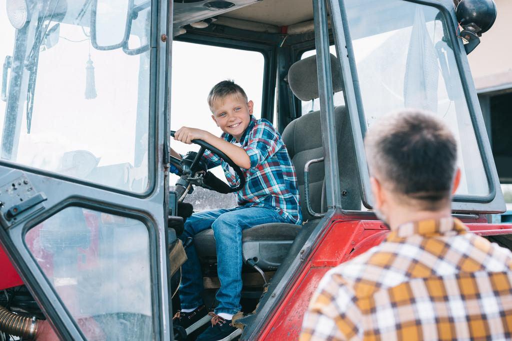Selektivní fokus otce při pohledu na šťastný syn sedí v traktoru - Fotografie, Obrázek