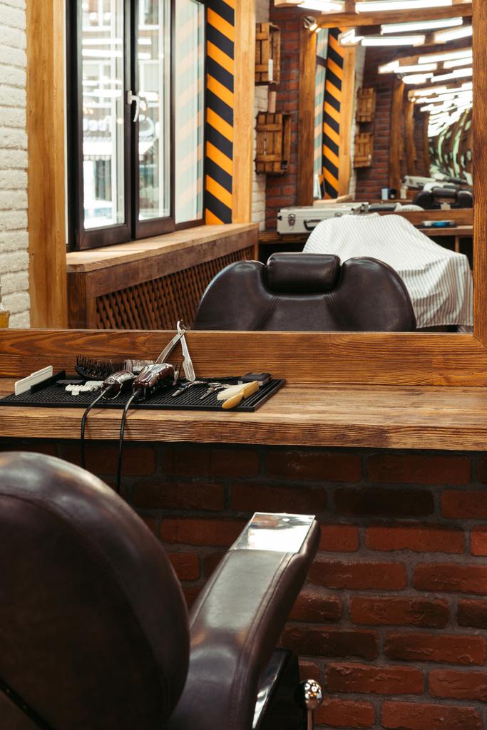 moderno interior de la barbería reflejado en espejo y herramientas de peluquería profesional en estante de madera
 - Foto, Imagen