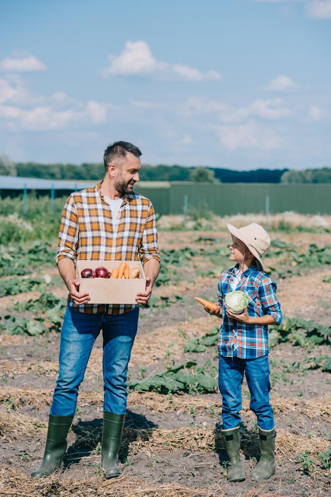 Šťastný otec a syn drží zralé zeleniny a usmívá se navzájem v poli  - Fotografie, Obrázek