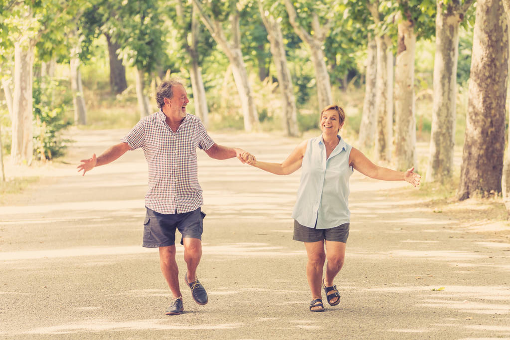 Ευτυχισμένο ζευγάρι ανώτερος στην αγάπη με τα πόδια και κρατώντας τα χέρια στο πάρκο - Φωτογραφία, εικόνα