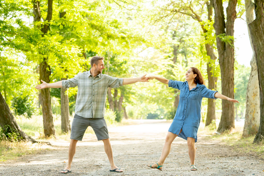 幸せなカップル ダンスと美しい緑豊かな公園で一緒に楽しんで - 写真・画像