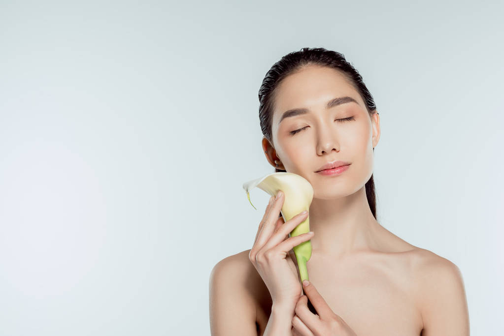 mooi Aziatisch meisje met gesloten ogen houden calla bloem, geïsoleerd op grijs, natuurlijke schoonheid - Foto, afbeelding