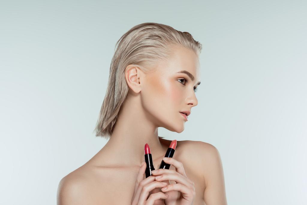 mooie blonde vrouw houden lippenstiften, geïsoleerd op grijs - Foto, afbeelding