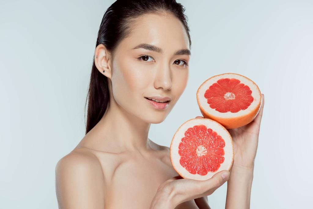 азіатська дівчина позує з грейпфрутовими половинками, ізольована на сірій, природній красі
 - Фото, зображення