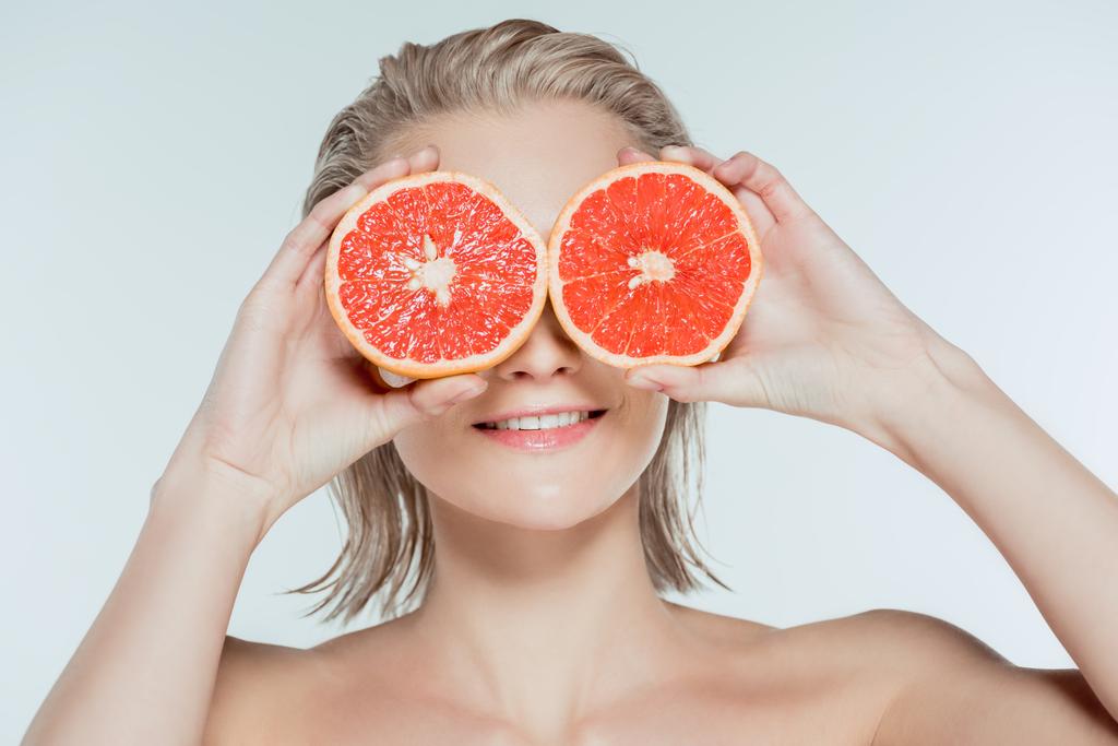 young woman holding grapefruit halves on eyes, isolated on grey - Photo, Image