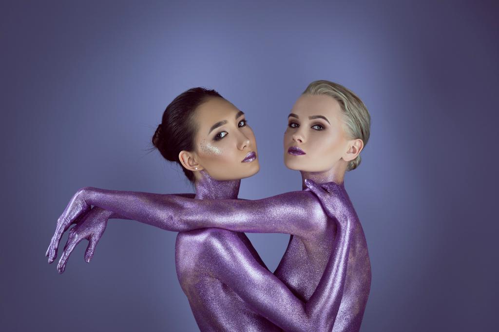 chicas atractivas multiculturales en brillo ultravioleta abrazándose, aisladas en púrpura
 - Foto, imagen