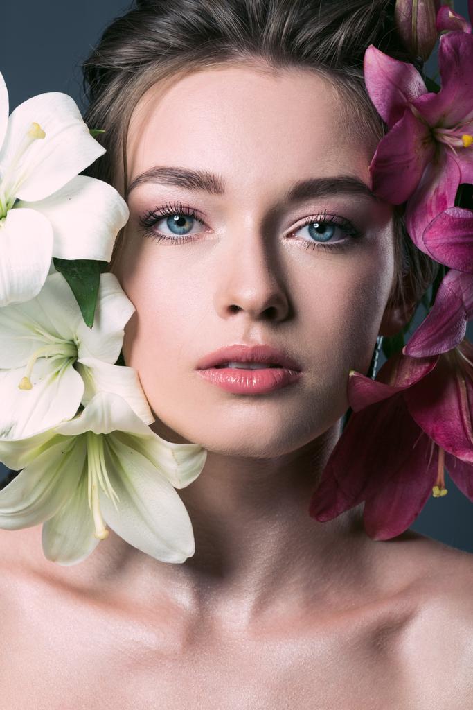 Close-up πορτρέτο του όμορφη νεαρή γυναίκα που περιβάλλονται με τα λουλούδια του κρίνου σε γκρι - Φωτογραφία, εικόνα