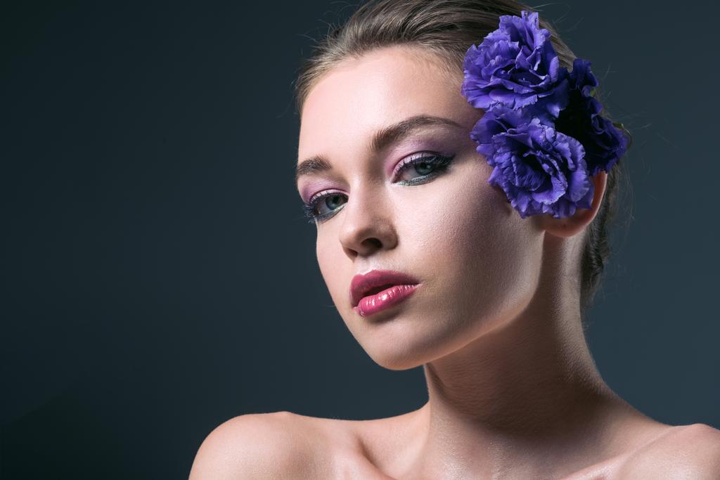 close-up portrait of seductive young woman with eustoma flowers behind ear looking at camera isolated on grey - Photo, Image