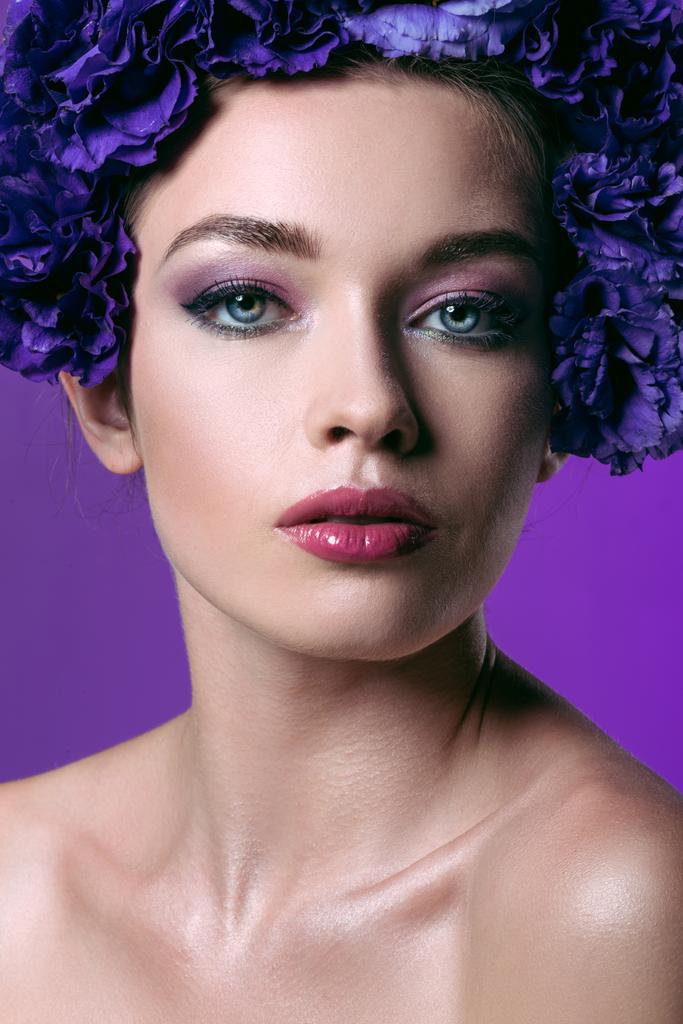 Nahaufnahme Porträt einer schönen jungen Frau mit Eustoma-Blumenkranz auf dem Kopf, die in die Kamera schaut, isoliert auf lila - Foto, Bild