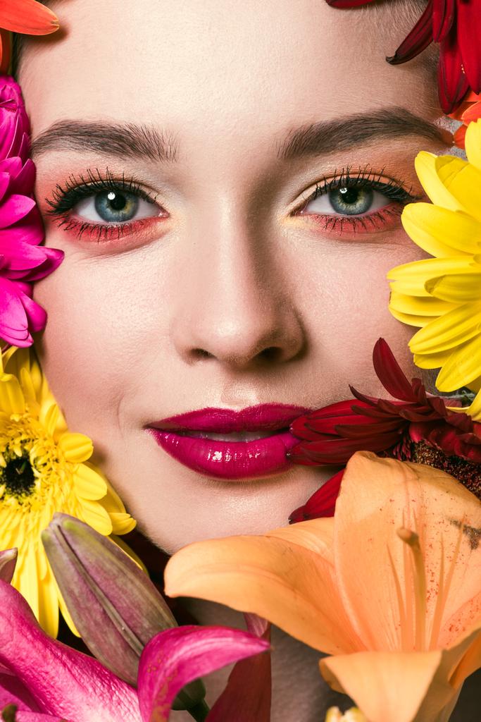крупным планом портрет красивой молодой женщины в окружении различных цветов, смотрящей в камеру
 - Фото, изображение
