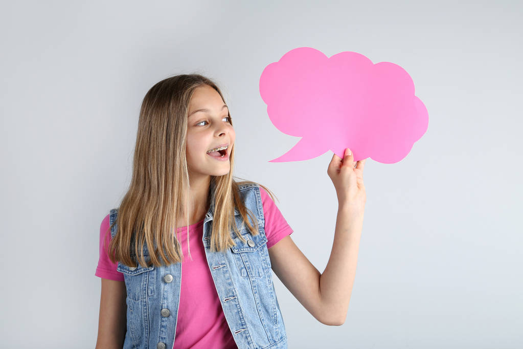 Chica joven sosteniendo la burbuja del habla sobre fondo gris
 - Foto, Imagen