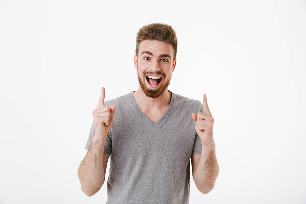 Image of handsome excited happy young man standing isolated over white wall background pointing. - Photo, Image