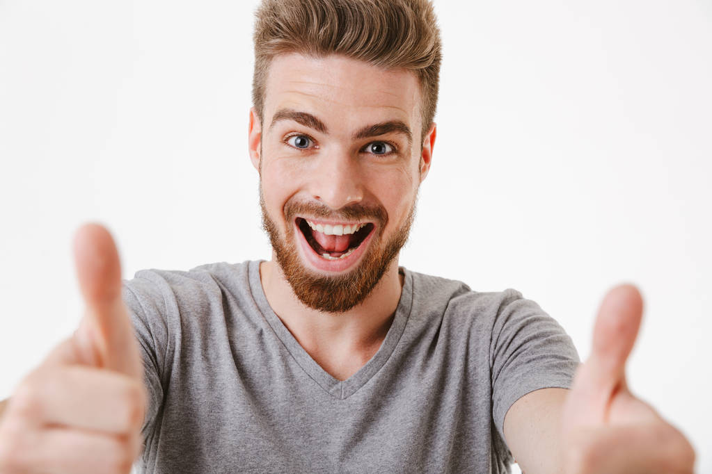Крупним планом портрет веселого молодого бородатого чоловіка, що показує великі пальці вгору жест ізольовані на білому тлі
 - Фото, зображення