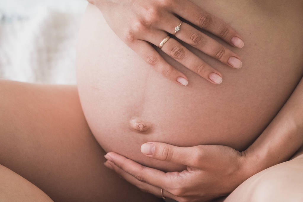 妊娠中の女性は赤ん坊のバンプの心臓の形で彼女の手を握っている。妊娠中の腹指ハートシンボル。妊娠の概念。ベビーシャワー - 写真・画像