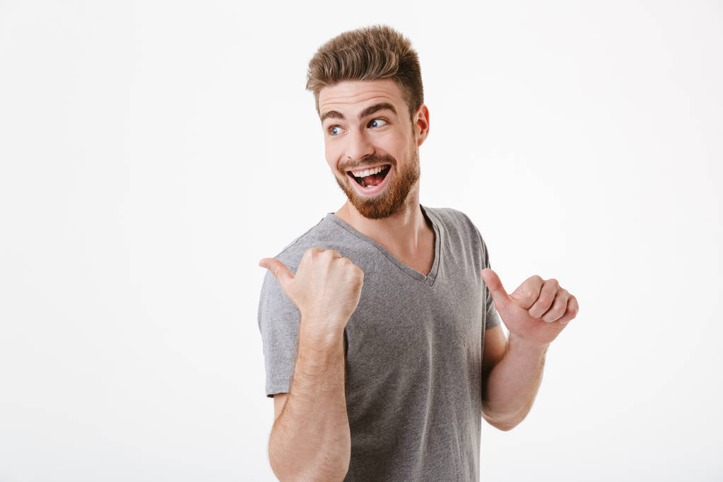 Image of handsome excited happy young man standing isolated over white wall background pointing. - Photo, Image