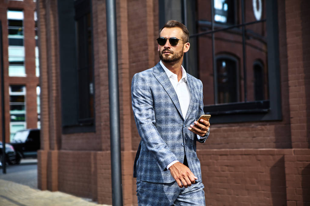 Porträt eines sexy, gut aussehenden Geschäftsmannsmodells im eleganten karierten Anzug, das auf der Straße geschäftliche Handygespräche auf dem Smartphone führt. Metrosexuelles Gehen - Foto, Bild
