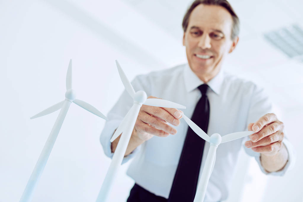 fröhlicher Mann berührt winzige weiße Windmühlengeneratoren - Foto, Bild