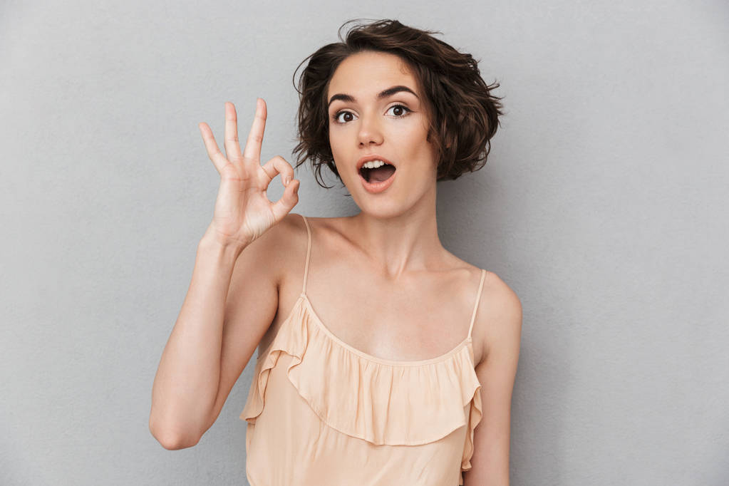 Портрет веселої молодої жінки, що показує ок жест ізольовано на сірому фоні
 - Фото, зображення