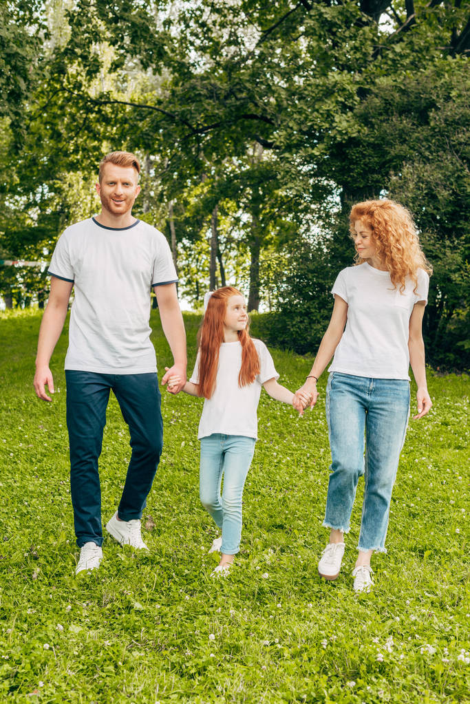 ευτυχισμένη οικογένεια με ένα παιδί, κρατώντας τα χέρια και τα πόδια μαζί στο πάρκο - Φωτογραφία, εικόνα