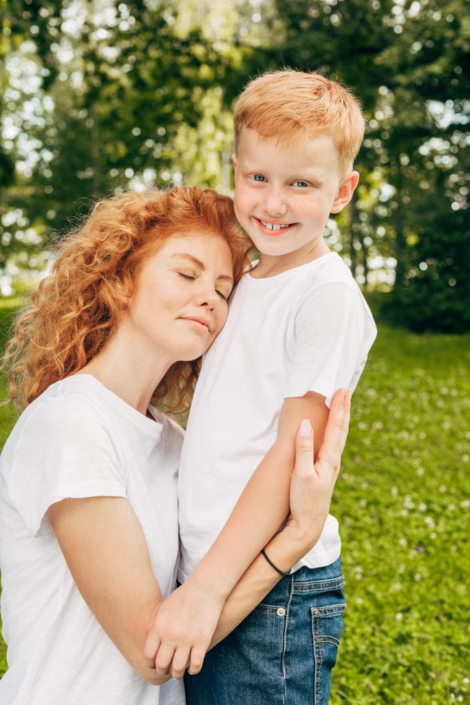ευτυχισμένος νέοι η μητέρα αγκαλιάζει αξιολάτρευτο μικρό γιο στο πάρκο - Φωτογραφία, εικόνα