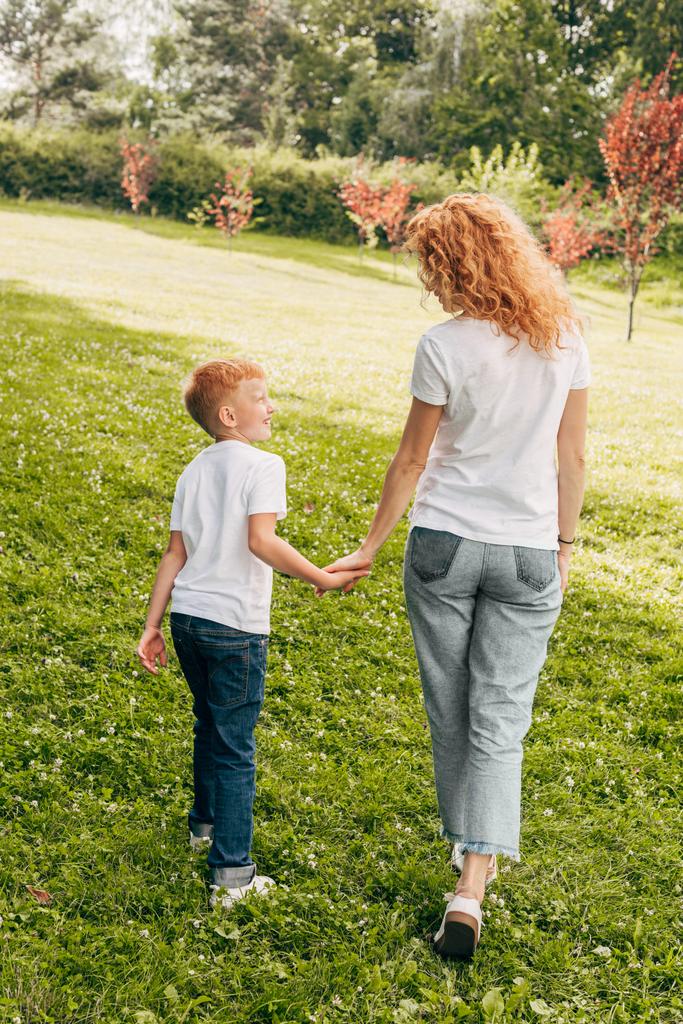 vue arrière de mère heureuse et fils tenant la main et marchant ensemble dans le parc
 - Photo, image