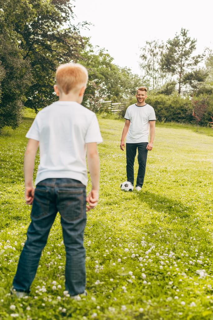 πατέρας και γιος παίζει με την μπάλα ποδοσφαίρου στο πράσινο γκαζόν στο πάρκο - Φωτογραφία, εικόνα