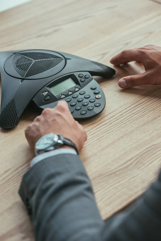 cropped shot of businessman pushing button of conference phone at workplace in office - Photo, Image