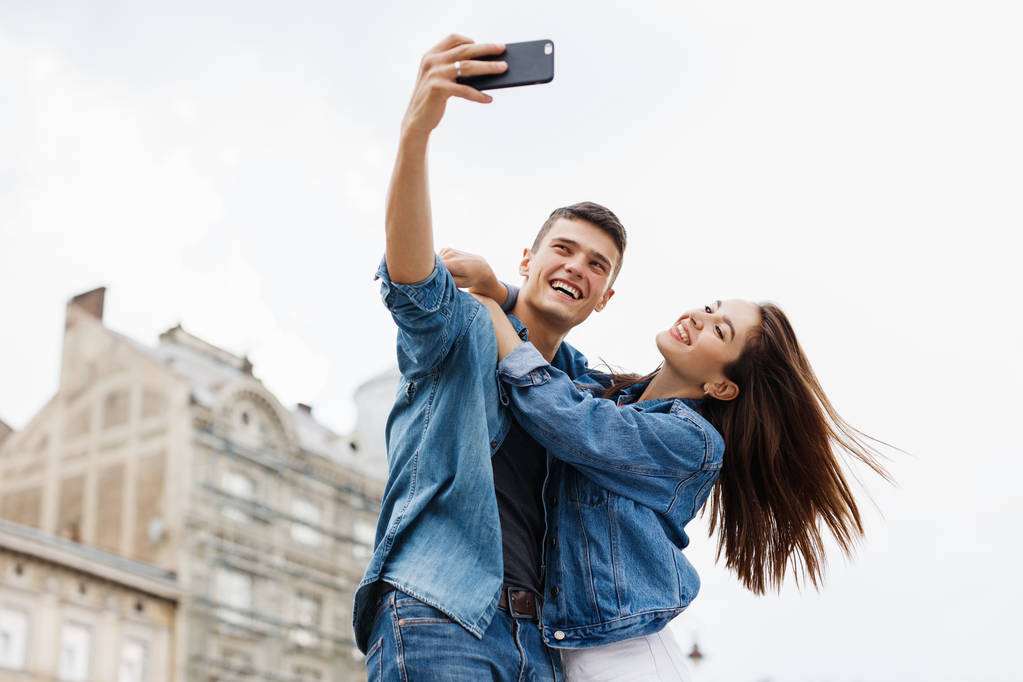 Couple prenant des photos dans la grande rue de la ville. Jeune homme souriant et femme heureuse faisant Selfie Photo sur téléphone portable. Haute résolution
. - Photo, image